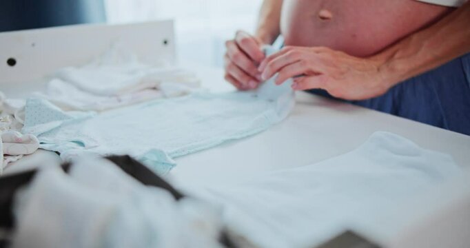 Pregnant woman folding newborn baby clothes on changing table, close-up view