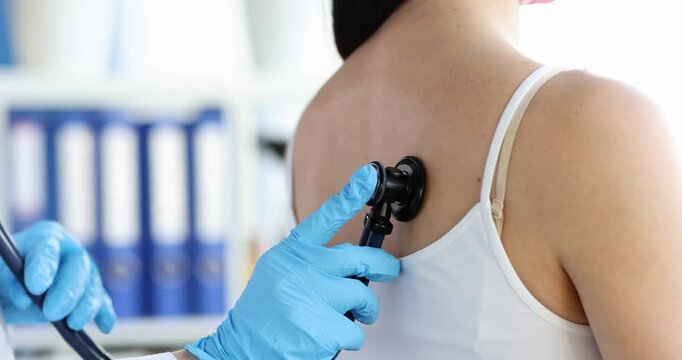 Doctor with stethoscope listens to woman breathing during examination in clinic. Wheezing in lungs when breathing in adult without fever concept