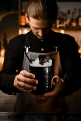Bartender presents a cocktail with a straw, disguised as an oil barrel.