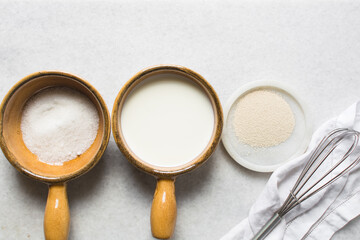 mise en place of ingredients for making bread, overhead view of ingredients for proofing yeast, yeast milk and sugar on a white marble countertop