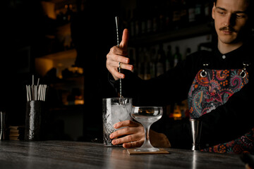 Masterful Chill. Bartender stirs an ice-filled cocktail with a master's spoon.