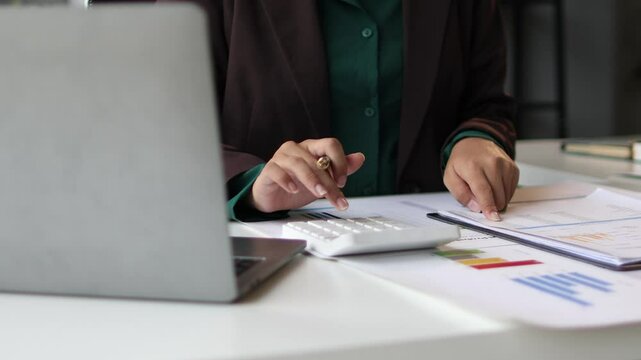 Accountant woman calculating finances in office. Professional female accountant working in an office, calculating finances, writing on documents, and using a laptop.
