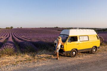 Young blonde woman enjoying the view in her retro yellow camper van at sunrise in Valensole lavender fields in Provence, France