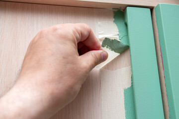 Hand of a person removing masking tape from furniture after painting