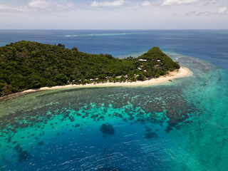 Aerial view of tropical island beach with shallow turquoise water and corals reefs seen from above....