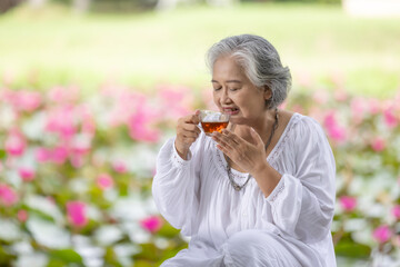 Fototapeta premium Elderly Woman Enjoying a Cup of Tea in a Lush Garden with Pink Water Lilies, Embracing Tranquility and Relaxation in Nature While Wearing a White Outfit