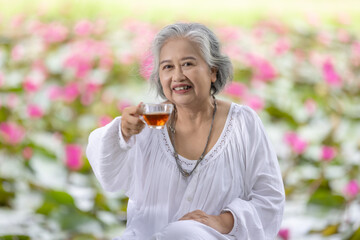 Fototapeta premium Elderly Woman Enjoying a Cup of Tea in a Lush Garden with Pink Water Lilies, Embracing Tranquility and Relaxation in Nature While Wearing a White Outfit