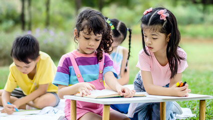 Little boy and girl were having fun drawing pictures and read book, Group of children playing and on sunny summer day in the park, holiday relaxation concept, picnic in summer park, outdoor education