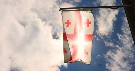 Sun rays break through the waving flag of Georgia against the backdrop of a blue sky with clouds. georgia independence day