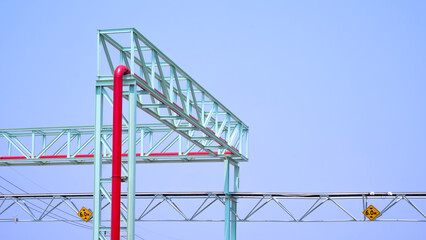 Overhead oil pipeline with metal rail and electric cable ladder tray outside of industrial building against blue sky background 
