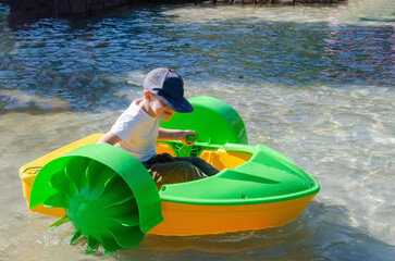 Kid playing rowing water paddle boat. Soft focus. A little girl rides a colorful boat on a pool in...