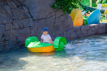 Kid playing rowing water paddle boat. Soft focus. A little girl rides a colorful boat on a pool in...