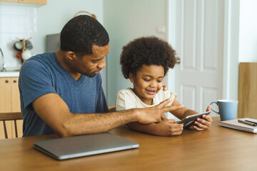 Black African American African American Father and son using tablet together at kitchen table, bonding over technology and having fun with a digital device.