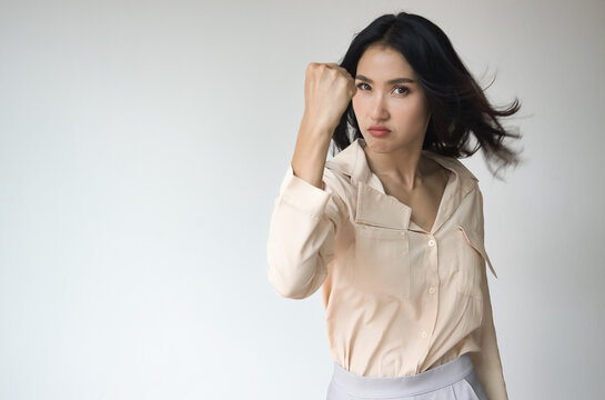 Angry upset unhappy young adult Asian woman with angry or furious expression, raising her threatening fist, ready to fight and punch right away - Powered by Adobe