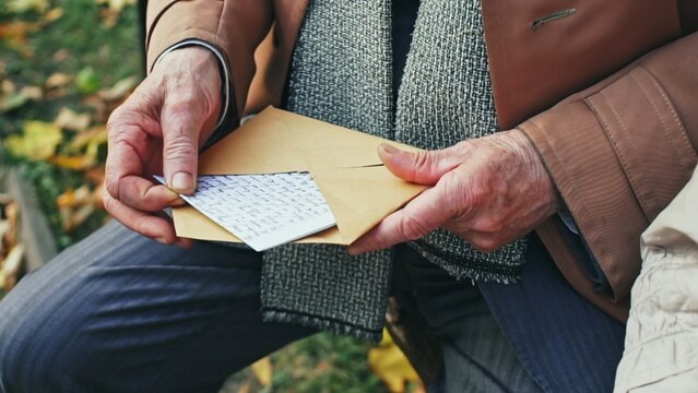 Elderly man opening handwritten letter in park