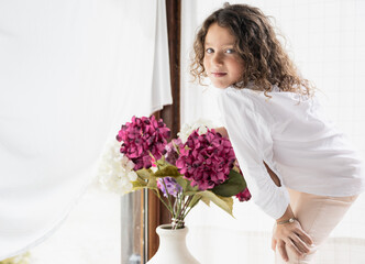 Young girl with curly hair posing by flowers, copy space.