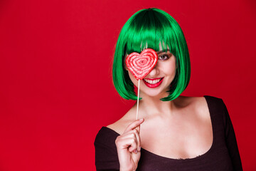 Woman with Green Hair Holding Heart Lollipop Over Eye. Young Caucasian woman with short green hair,...
