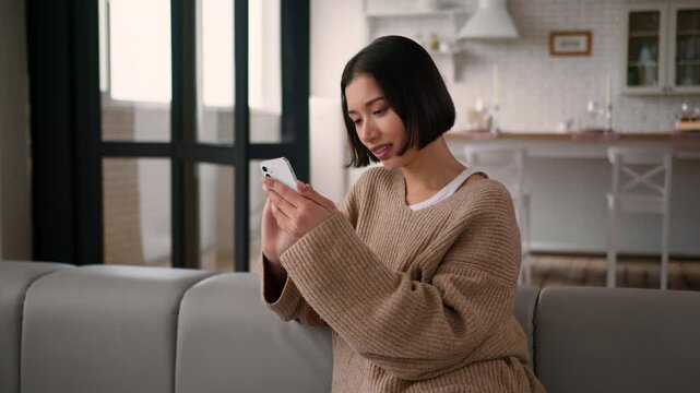 Caucasian hispanic woman girl satisfied lady homeowner tenant buyer female in casual on couch using mobile phone app shopping online order delivery browsing internet typing message smile home weekend