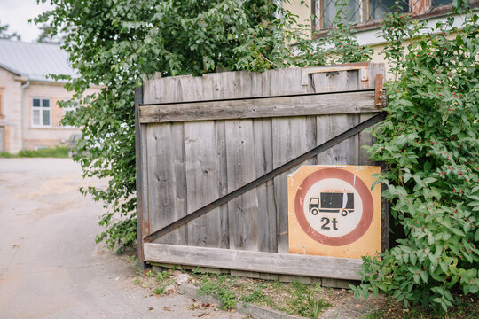 Riga, Latvia - July 19, 2024 - Wooden gate with a sign indicating a 2-ton weight limit for vehicles, surrounded by greenery and a nearby building.
