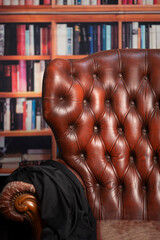 Studio shot of an antique brown leather Chesterfield empty armchair in front of a bookcase