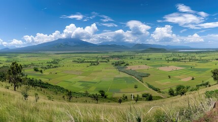 Obraz premium A breathtaking panoramic view of a large, green volcano with a fluffy white cloud hovering above its peak. Lush forests surround the volcano, and the sky is a bright blue with white fluffy clouds