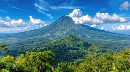 Fototapeta premium A breathtaking panoramic view of a large, green volcano with a fluffy white cloud hovering above its peak. Lush forests surround the volcano, and the sky is a bright blue with white fluffy clouds