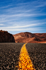 The open road leading through the stunning Moroccan desert landscape. With a vivid yellow line guiding the way, the rugged mountains and expansive sky create a perfect scene.