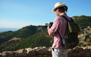 Man photographing mountainous landscape on a sunny day with backpack and hat