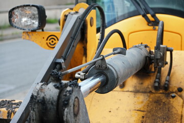 Hydraulic cylinder in a construction vehicle. Part of a construction machine mechanism. Frontal view. Shiny surface. Yellow color.