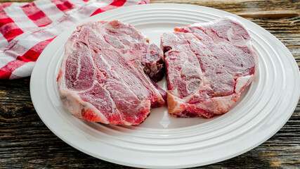 Two raw frozen lamb chops on white plate with red checkered napkin