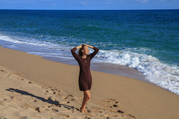 a beautiful girl in a brown dress is walking on the sandy beach and enjoying the sea view