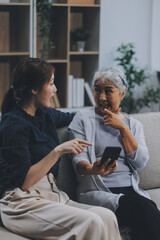 Cheerful mother and pretty teenager kid relaxing at cozy home, using mobile phone for Internet communication, resting on sofa with digital gadget, enjoying leisure, looking at camera