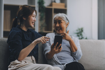 Cheerful mother and pretty teenager kid relaxing at cozy home, using mobile phone for Internet communication, resting on sofa with digital gadget, enjoying leisure, looking at camera