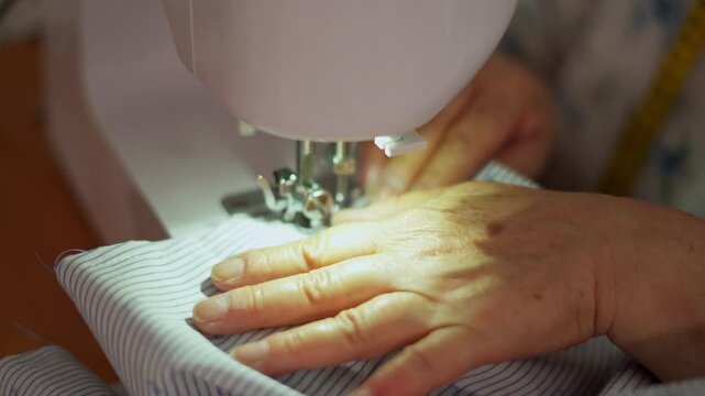 A close-up shot of a senior woman&rsquo;s hands sewing blue striped fabric with a white sewing machine. retirement concept