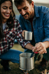 Beautiful and romantic young man and woman preparing hot coffee and tea beverage portable stove sitting outside the tent during hiking adventure