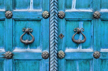 Old wooden turquoise door with aged metal door handles and rivets. Architectural background