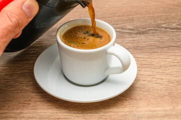 Pouring coffee. White cup, cezve on the wooden table