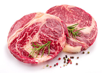 Raw beef steaks with herbs and spices ready for cooking on white background.