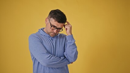 Defiant senior man with glasses on a yellow background crossing his arms in refusal