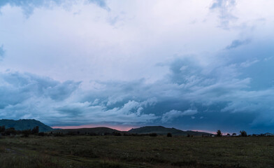 The red sunset shines through between the mountains and dark clouds.