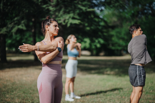 Group of young adults performing stretching exercises outdoors in a park. They are dressed in athletic wear and enjoying a sunny day workout.