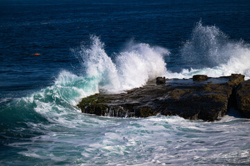 2023-12-31 WAVESS CRASHING ON THE ROCKY SHORELINE SPRAYING WATER ALONG THE COASTLINE WITH MULTIPLE SWIMMERS IN THE BACKGROUND IN LA JOLLA CALIFORNIA NEAR SAN DIEGO