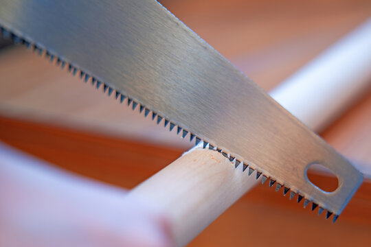 Manually sawing a wooden shovel handle with a hand saw
