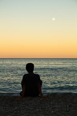a lonely man sits on the seashore at sunset