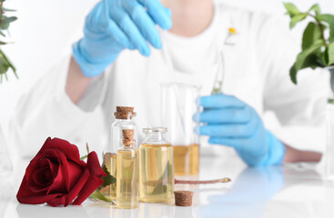 Aromatherapy product. Scientist developing essential oils at white table in laboratory, focus on bottles and rose