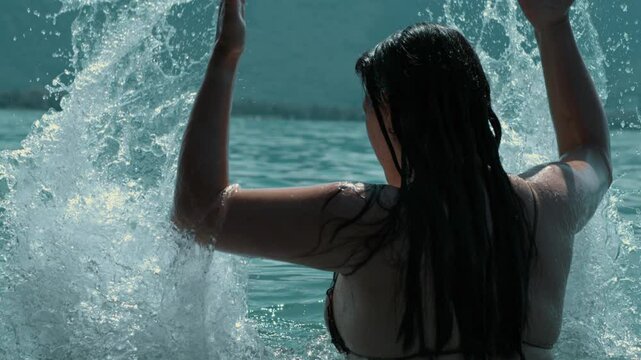 Woman in water splashing water in the air with arms raised, blue lake, high-speed slow-motion capture, summer energy, refreshing outdoors, freedom, dynamic movement, serene nature