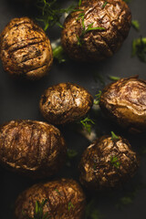 Baked small potatoes with herbs on a black plate close-up.