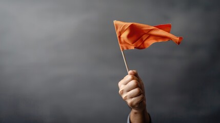 A hand holds a waving orange flag against a dark gray background with copy space, illustrating a leader's vision for achievement and victory.