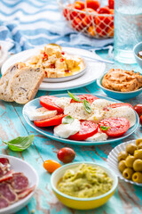 Picnic table with assorted appertizers, raw vegetables, cheese, dips, baguette and pastrami and serrano platter