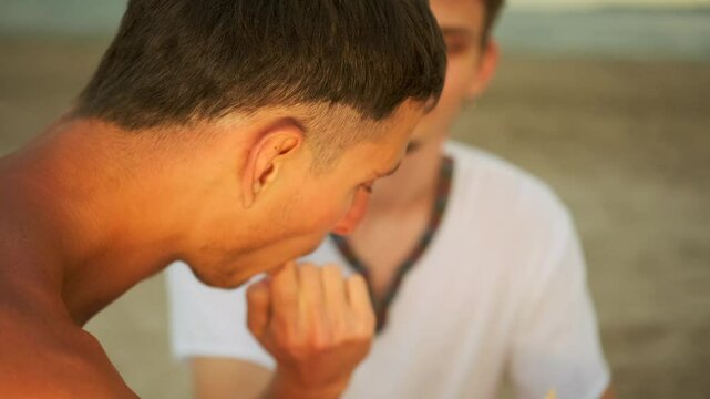 Young guy licks his friend's finger sauce and eats sushi rolls while relaxing on the beach, close-up.
